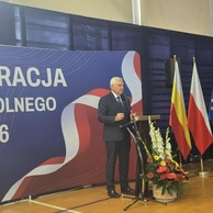 Zdjęcie przedstawiające mężczyznę w garniturze przemawiającego z podium, za którym widoczne są flagi Białegostoku, Polski i Unii Europejskiej.