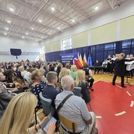 Zdjęcie przedstawiające chór występujący na scenie, widziany z perspektywy publiczności, z transparentem