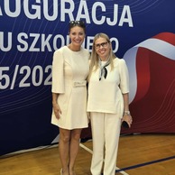 Zdjęcie przedstawiające dwie uśmiechnięte kobiety, stojące razem na tle transparentu z napisem