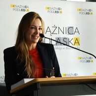 Iwona Gaweł - dyrektor Książnicy Podlaskiej - przemawia przy mównicy. W tle baner z logo Książnicy Podlaskiej.