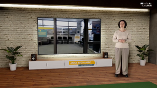 Kobieta stoi w wirtualnym studiu telewizyjnym przed dużym ekranem. Ekran pokazuje wnętrze jakiegoś pomieszczenia, być może poczekalni, z rzędem czarnych krzeseł. Kobieta ma na sobie jasny sweter i szare spodnie. Stoi po prawej stronie ekranu. Pod ekranem znajduje się szafka RTV z głośnikami po bokach, a na niej widoczna jest plakietka z napisem ANNA KOCHANIEC i pod spodem mniejszymi literami DZIAŁ ZESPOŁÓW SPECJALNYCH. Ściana za ekranem wygląda jak ściana z czerwonej cegły. Po obu stronach mebla RTV i ekranu znajdują się doniczkowe rośliny. U góry po prawej stronie widać logo z napisem KSIĄŻNICA PODLASKA. Podłoga jest drewniana.