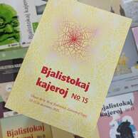 Zdjęcie przedstawia okładkę 15. numeru czasopisma „Bjalistokaj Kajeroj” w języku esperanto. Okładka jest w odcieniach żółci z geometrycznym wzorem przypominającym sieć lub pajęczynę w kolorze różowym. Na środku widnieje duży czerwony napis:
„Bjalistokaj kajeroj No 15”
Pod spodem mniejszym tekstem:
„Okaze de la 26-a Bjalistokaj ZamenhofTagoj 12–15 de decembro 2025”