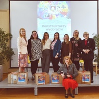 Pamiątkowe zdjęcie grupowe ośmiu uczestniczek seminarium na scenie. Przed nimi ułożone są pudełka z nagrodami i zestawami startowymi.
