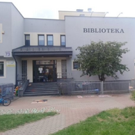 Frontowa elewacja budynku Filii nr 9 Książnicy Podlaskiej przy ul. Gajowej 73 w Białymstoku. Dwupiętrowy budynek z jasnoszarą elewacją, z widocznym napisem „BIBLIOTEKA