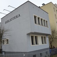Widok bocznej i częściowo frontowej elewacji budynku Filii nr 9 Książnicy Podlaskiej przy ul. Gajowej 73 w Białymstoku. Na pierwszym planie dominuje jasnoszara ściana boczna z napisem „BIBLIOTEKA